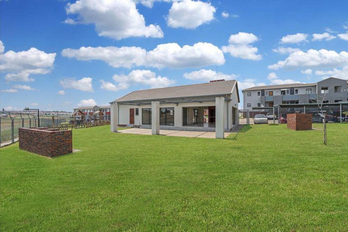 Rear view of the townhouse featuring a spacious lawn, a covered patio area, and a built-in brick braai facility.