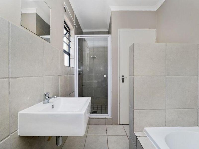 A functional bathroom featuring a wall-mounted basin, a separate glass-enclosed shower, and neutral floor-to-ceiling tiling.