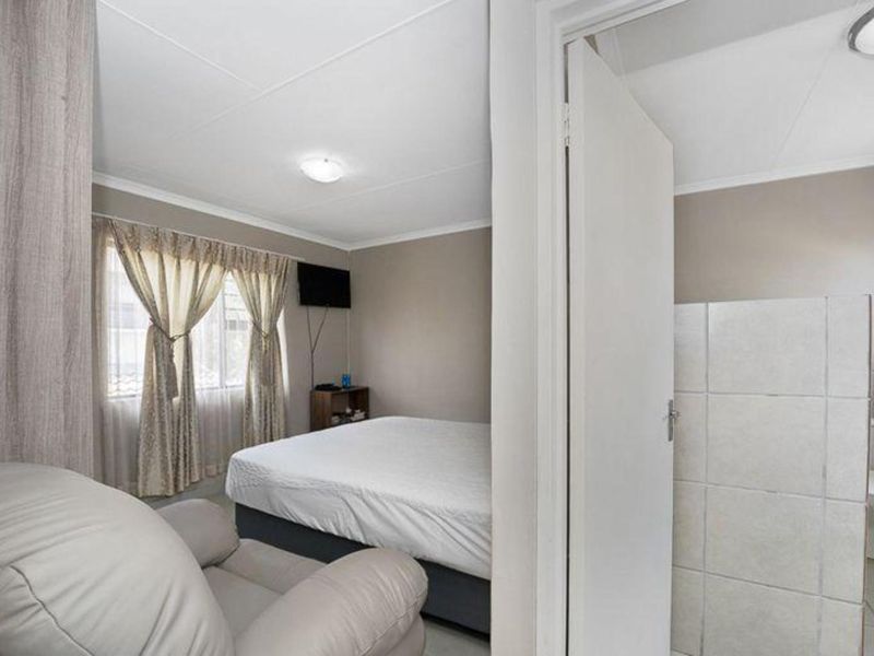 A bedroom featuring a neutral color palette, tiled flooring, and an adjoining bathroom area with a privacy partition.