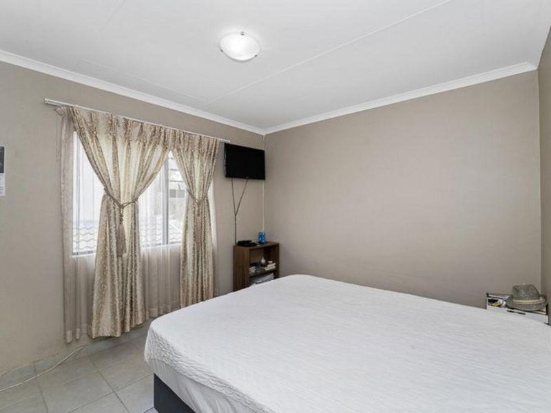 A standard bedroom featuring tiled flooring, neutral wall paint, and a window with curtain fixtures.