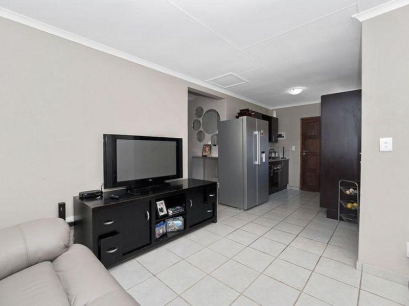 An open-plan living area featuring tiled flooring, neutral wall tones, and a compact kitchen space with dark cabinetry.