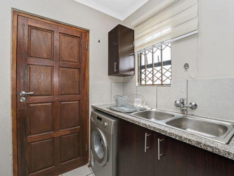 Functional laundry area featuring a double stainless steel sink, granite-look countertop, dark wood cabinetry, and a dedicated space for a front-loading washing machine.