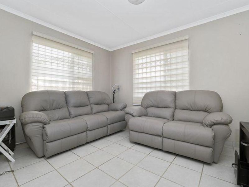A bright living room featuring neutral tiled flooring, coved ceilings, and dual windows fitted with modern roller blinds.
