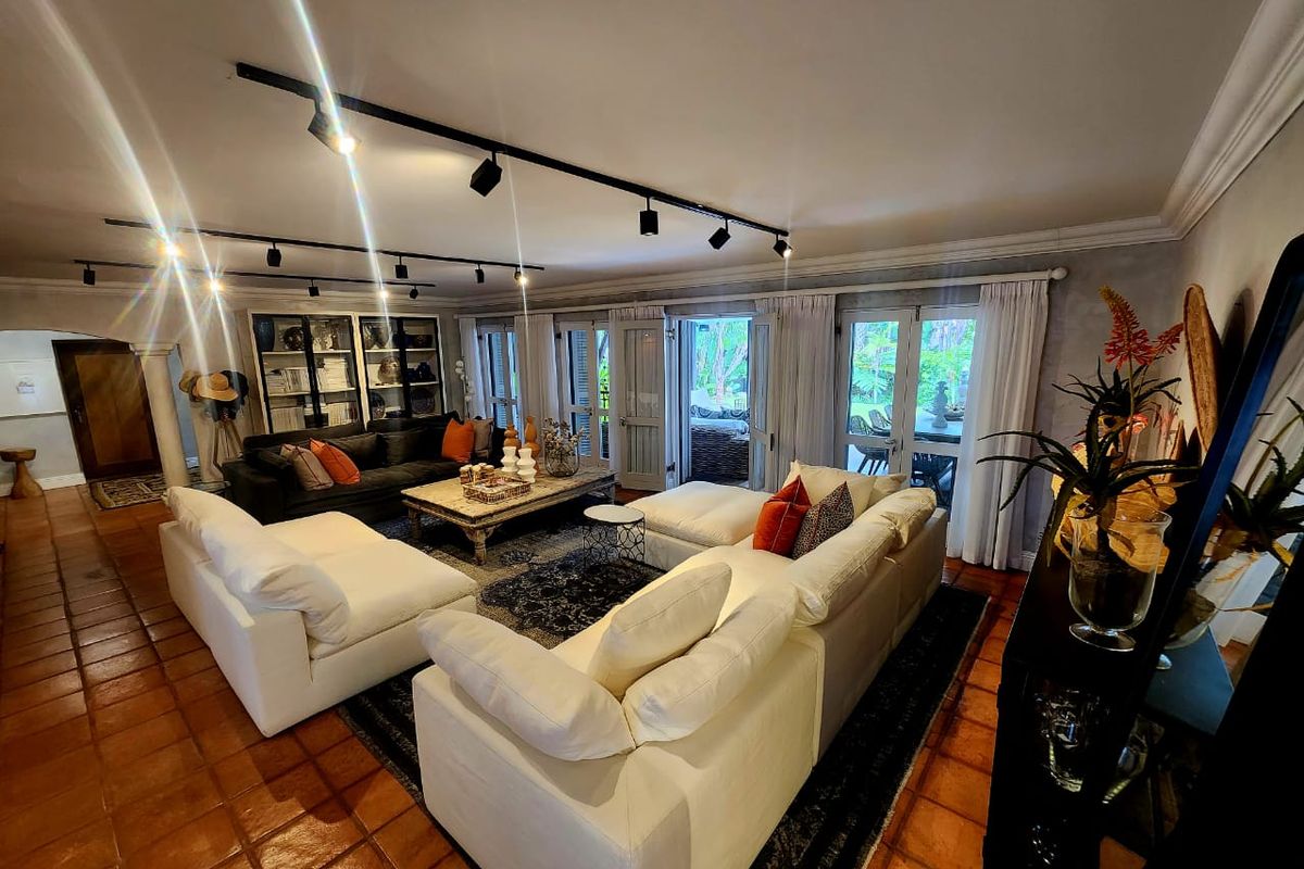 Spacious living room featuring terracotta floor tiles, track lighting, and multiple glass-paned double doors providing direct access to the outdoor patio area.