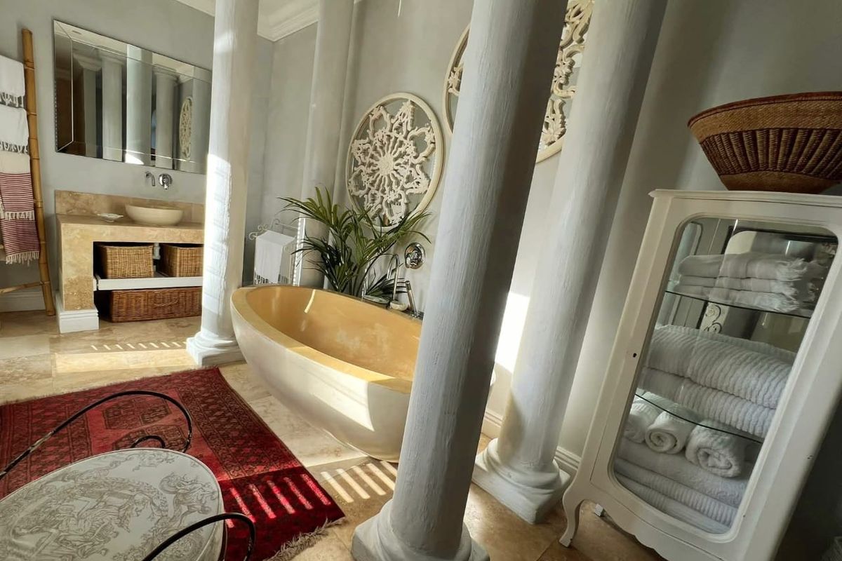 A spacious bathroom featuring a freestanding bathtub, stone-topped vanity with vessel sink, and decorative architectural columns.