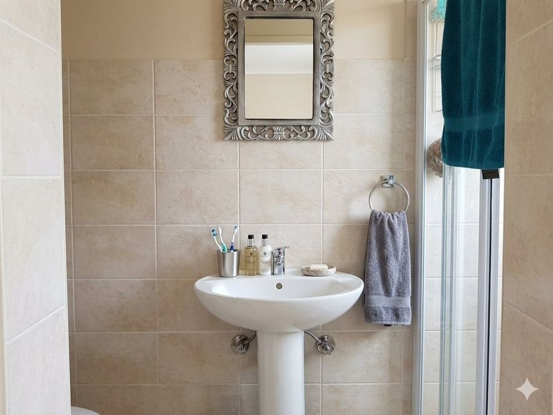 A clean bathroom featuring a pedestal basin with a chrome mixer tap and neutral wall tiling, adjacent to a shower enclosure.