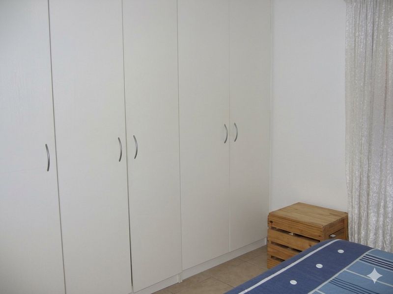 A bedroom featuring white built-in cupboards with modern handles and tiled flooring.