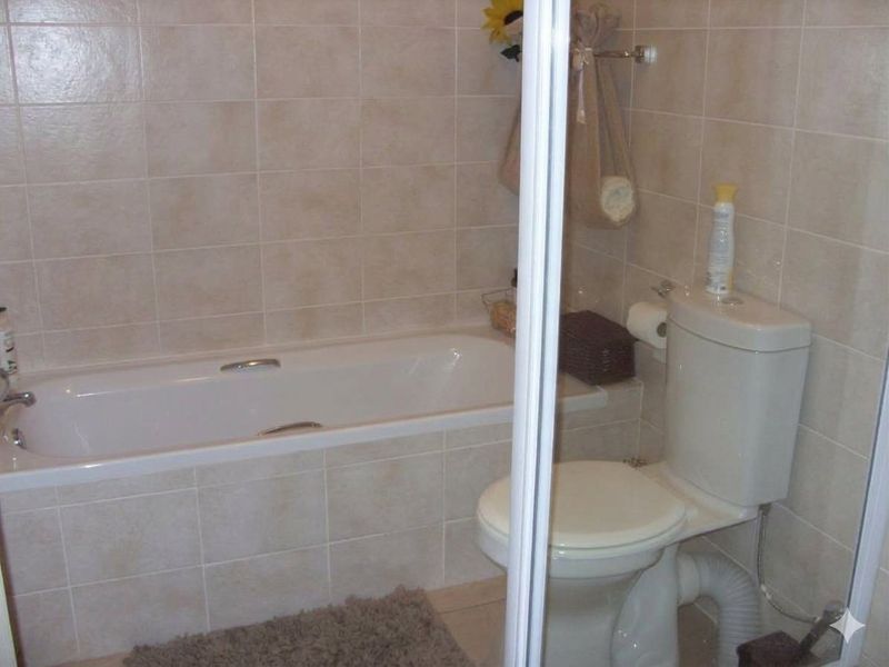 A functional bathroom featuring a built-in bathtub with tiled surround and a standard toilet, finished with neutral ceramic wall tiles.