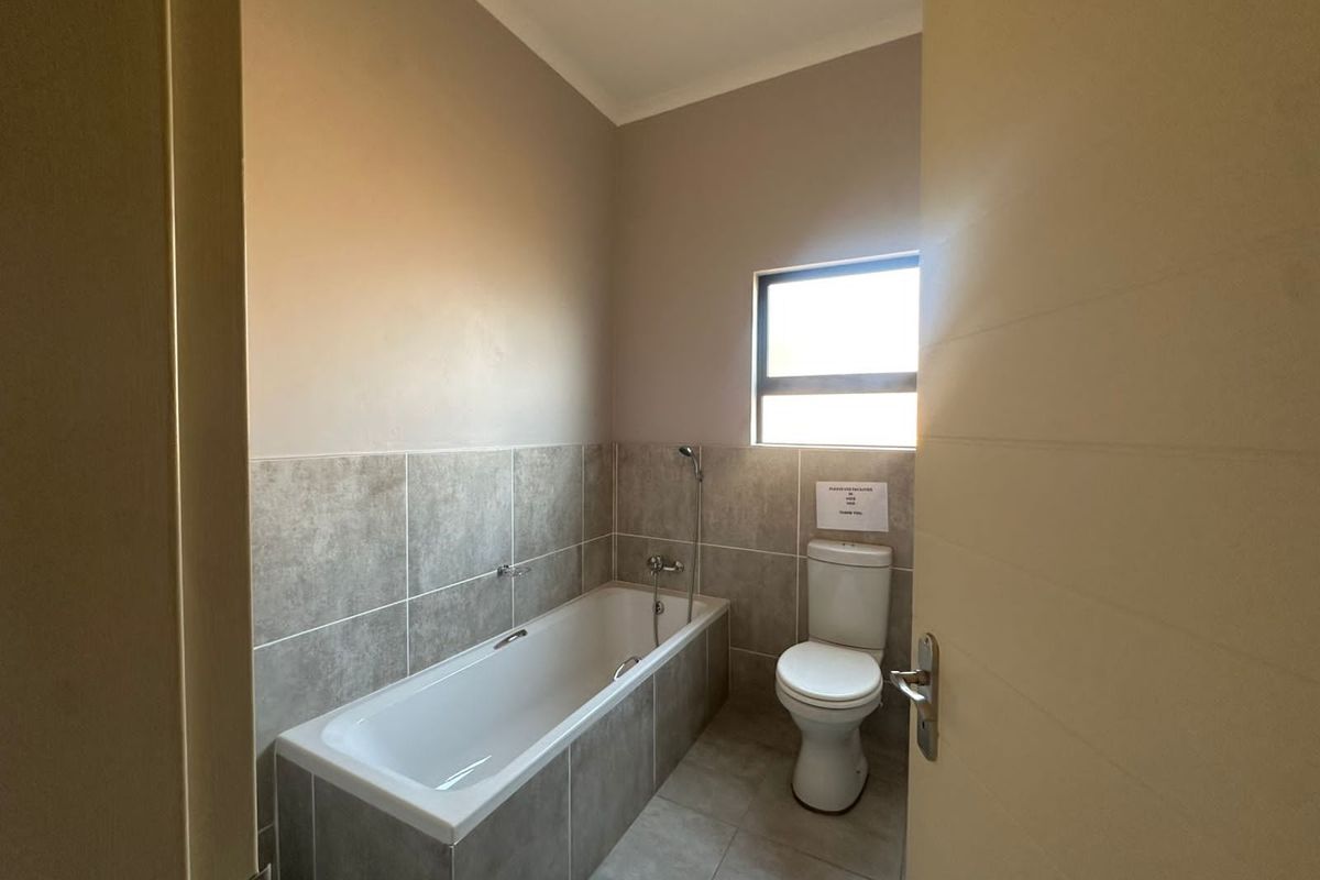 A clean, modern bathroom featuring a built-in bathtub with shower mixer and a standard toilet, finished with neutral grey wall and floor tiles.