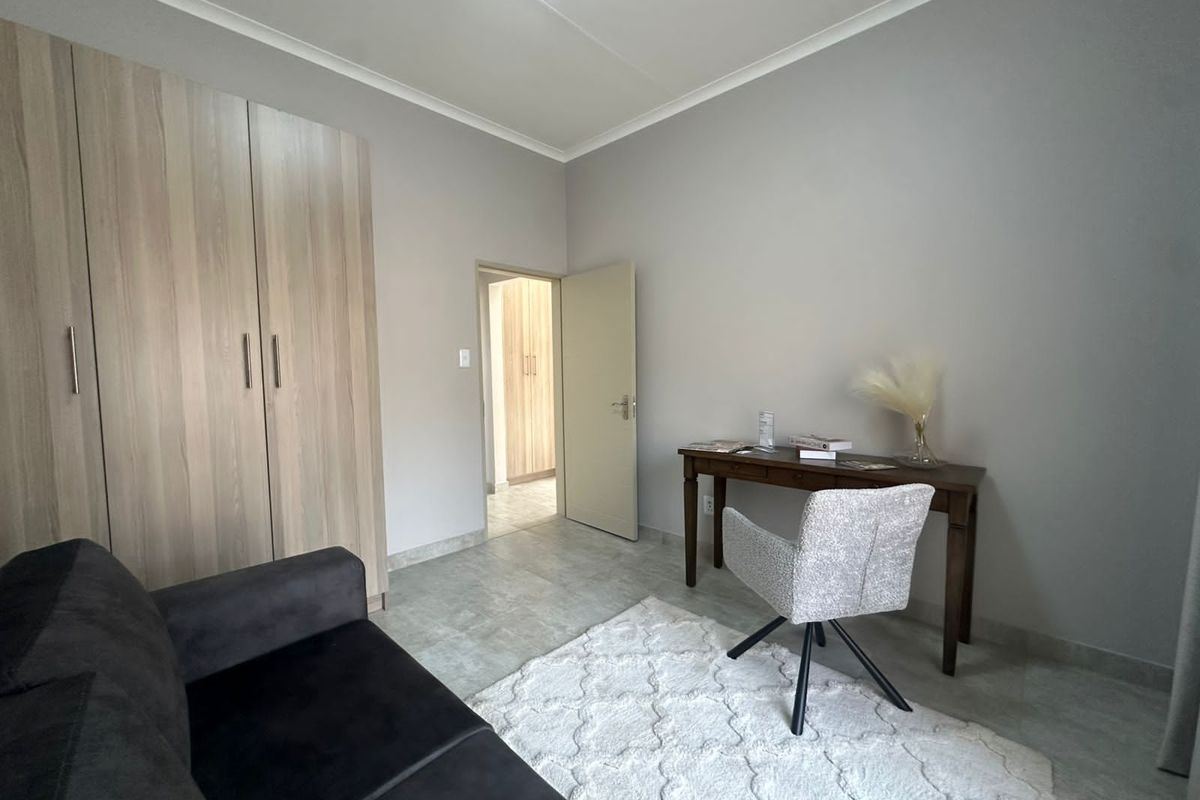 A bedroom featuring built-in wooden cupboards, tiled flooring, and neutral wall finishes, providing a clean and functional living space.
