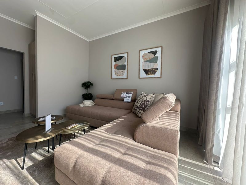 A well-lit living room featuring neutral wall tones, tiled flooring, and large windows with curtains, creating a comfortable and inviting atmosphere.