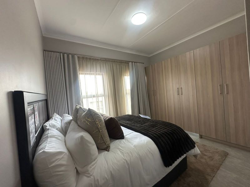 A well-maintained bedroom featuring extensive built-in wooden cabinetry, neutral wall finishes, and large windows with floor-to-ceiling curtains.