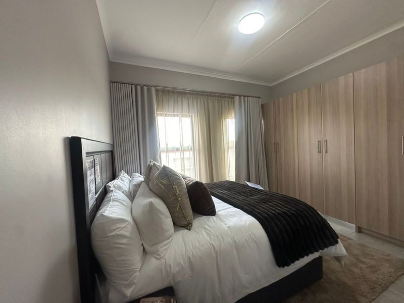 A well-maintained bedroom featuring built-in wooden wardrobes, neutral wall finishes, and large windows with curtain tracks.