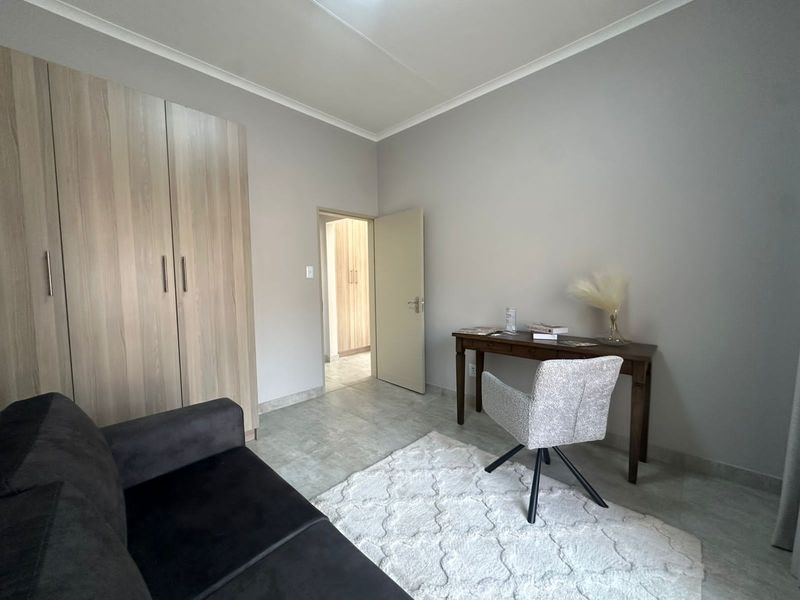 A bedroom featuring built-in wooden cupboards, tiled flooring, and neutral wall finishes, providing a clean and functional living space.