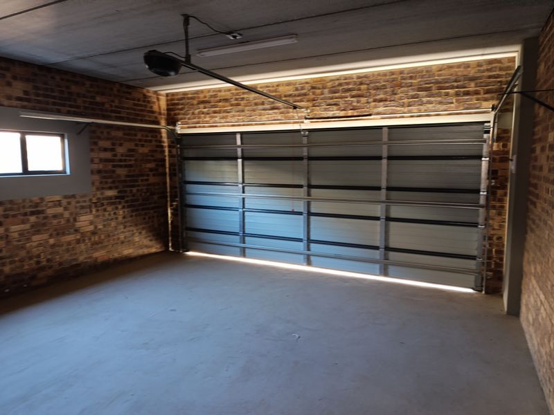 A spacious, clean garage featuring exposed brick walls, a concrete floor, and an automated sectional garage door.