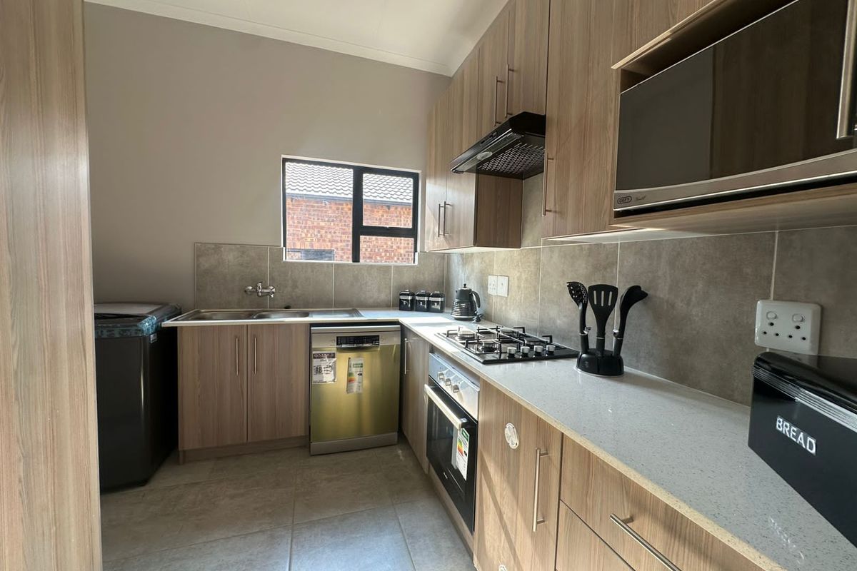 Modern kitchen featuring wood-look cabinetry, stone countertops, built-in gas hob, oven, extractor fan, and integrated space for a dishwasher and washing machine.