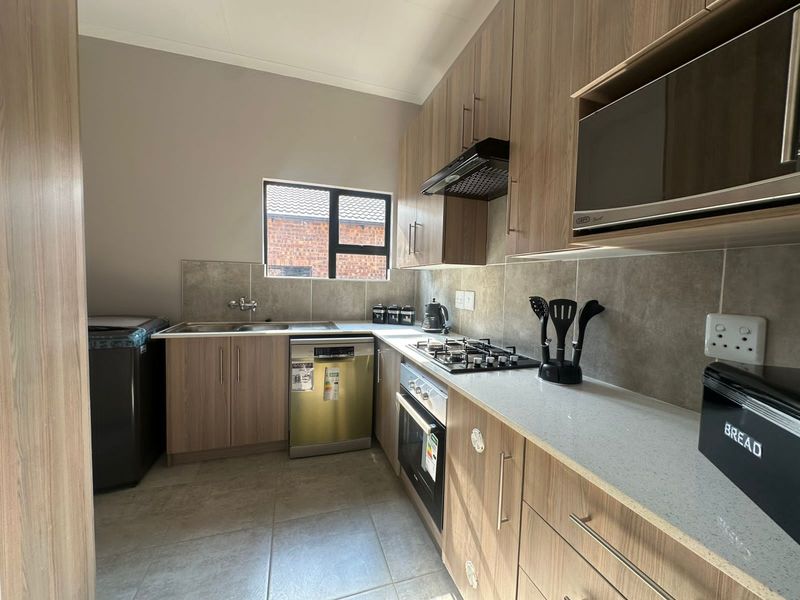 Modern kitchen featuring wood-look cabinetry, stone countertops, built-in gas hob, oven, extractor fan, and integrated space for a dishwasher and washing machine.