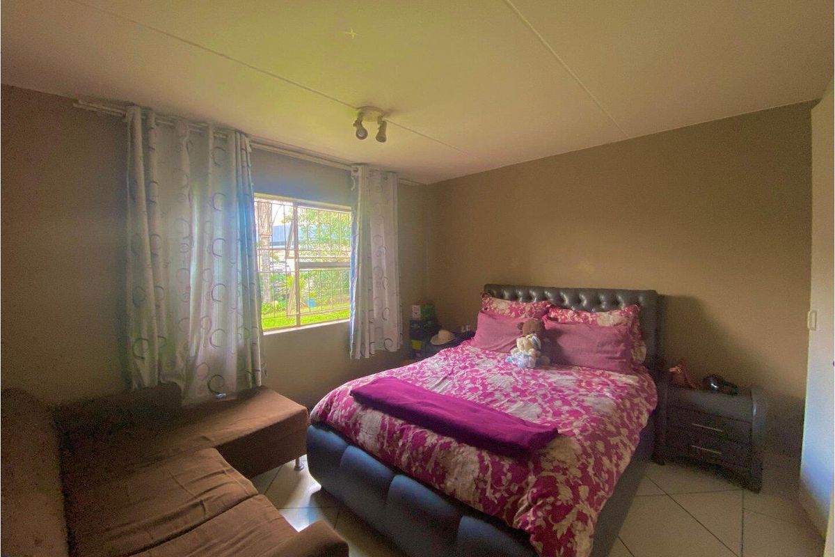 A bedroom featuring tiled flooring and a window with security bars, providing natural light to the space.