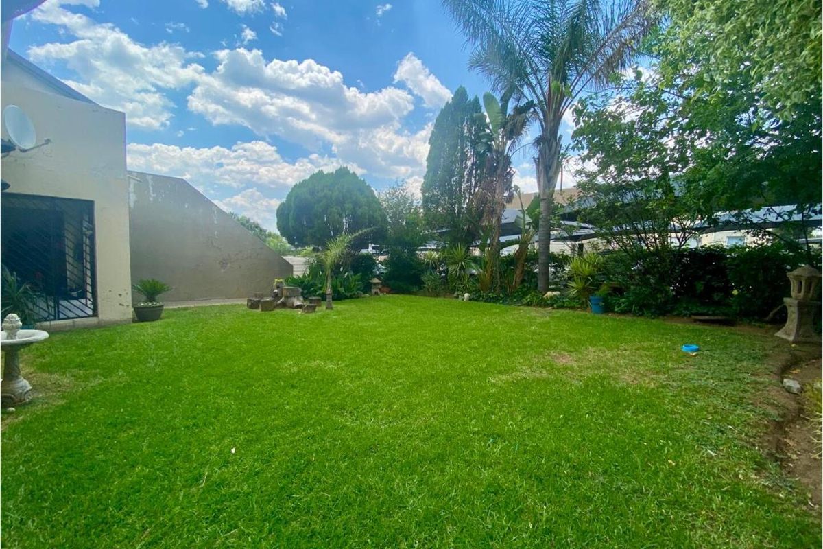 A private rear garden featuring a well-maintained lawn, mature trees, and established landscaping, providing a peaceful outdoor space for the apartment.