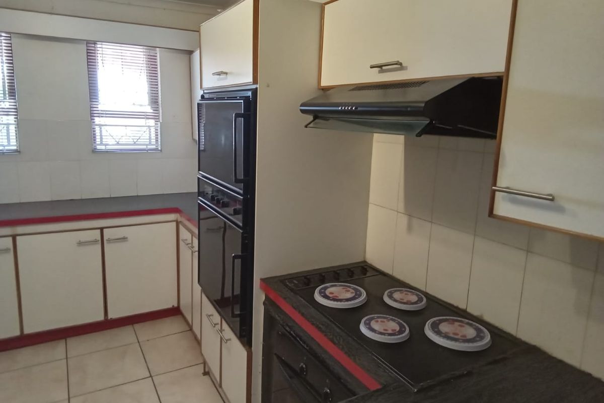 A functional kitchen featuring built-in cabinetry, an integrated oven, extractor fan, and electric hob with tiled flooring and splashbacks.