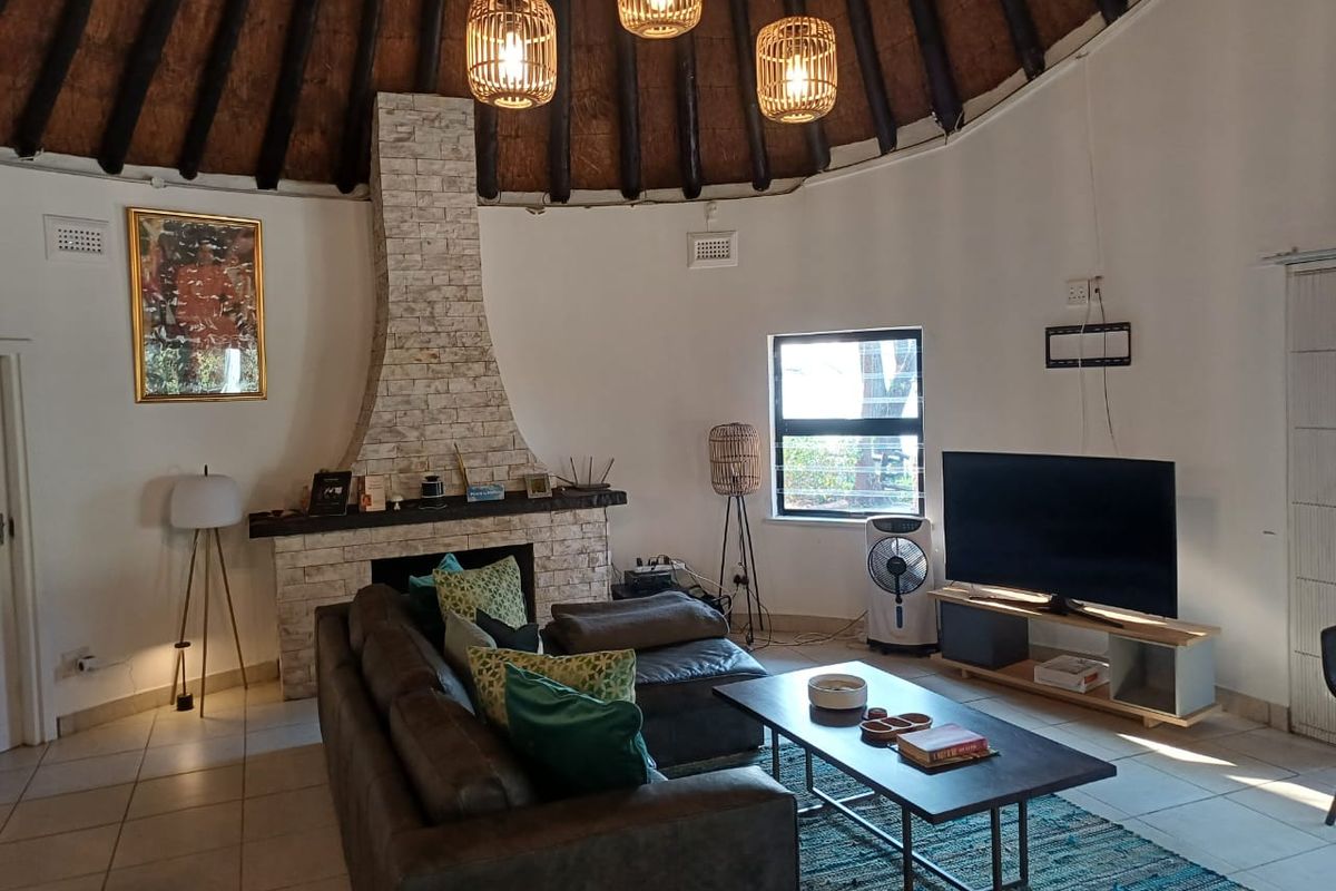 Spacious living room featuring a unique circular layout with a high thatched roof, exposed timber rafters, and a prominent stone-clad fireplace.