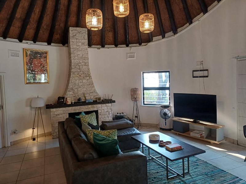 Spacious living room featuring a unique circular layout with a high thatched roof, exposed timber rafters, and a prominent stone-clad fireplace.