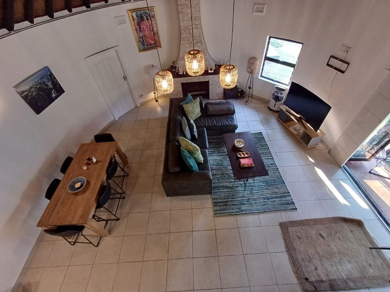 Spacious open-plan living and dining area featuring tiled floors, a central fireplace with stone surround, and high vaulted ceilings with natural light.