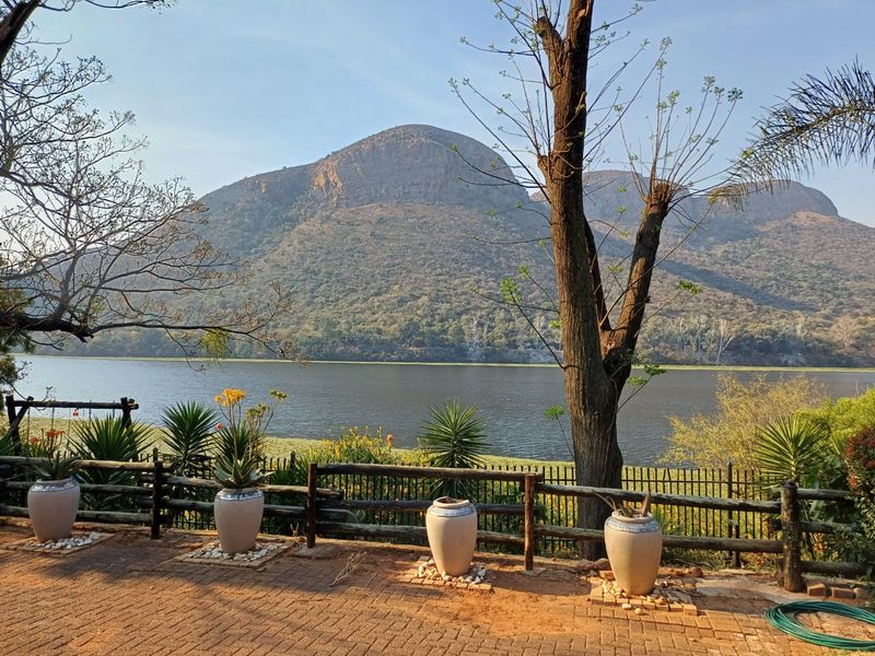 Scenic outdoor view featuring a paved patio area overlooking a tranquil lake and mountain landscape.