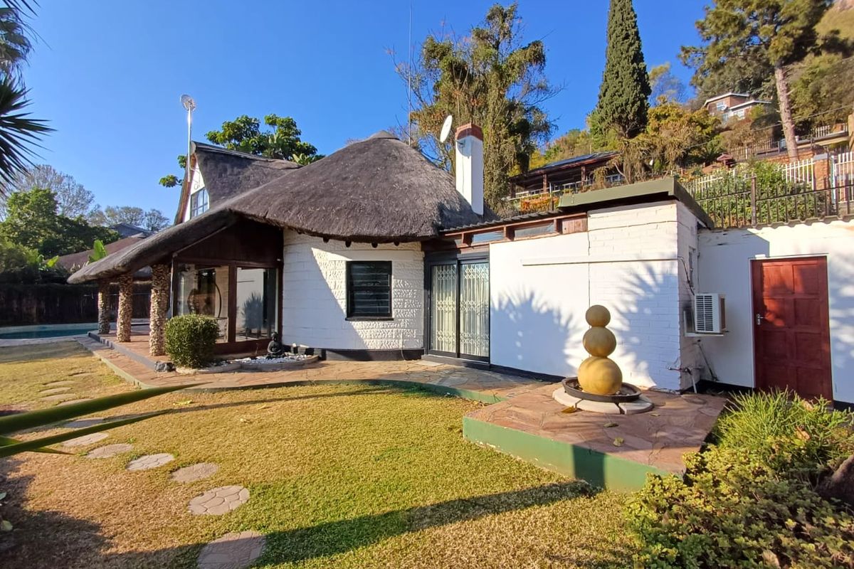 Rear view of a charming thatched-roof house featuring a stone patio, landscaped garden, and integrated outdoor water feature.