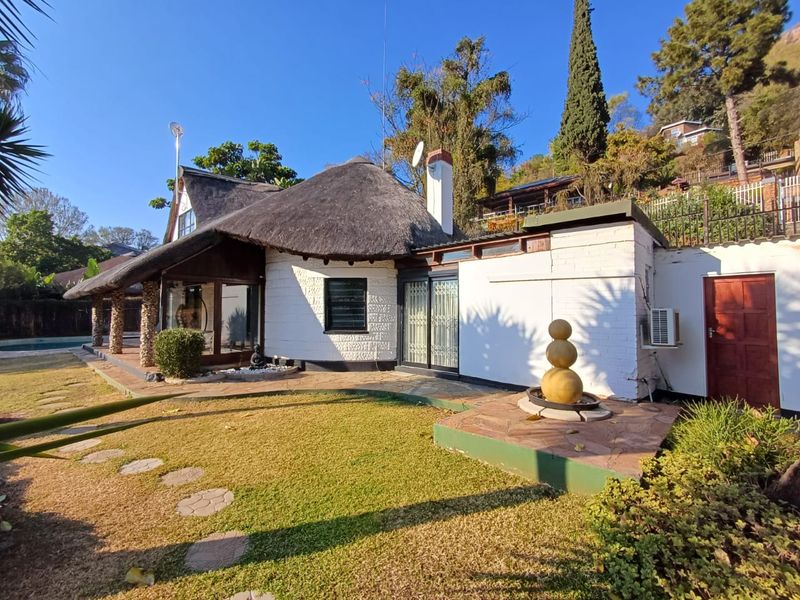 Rear view of a charming thatched-roof house featuring a stone patio, landscaped garden, and integrated outdoor water feature.