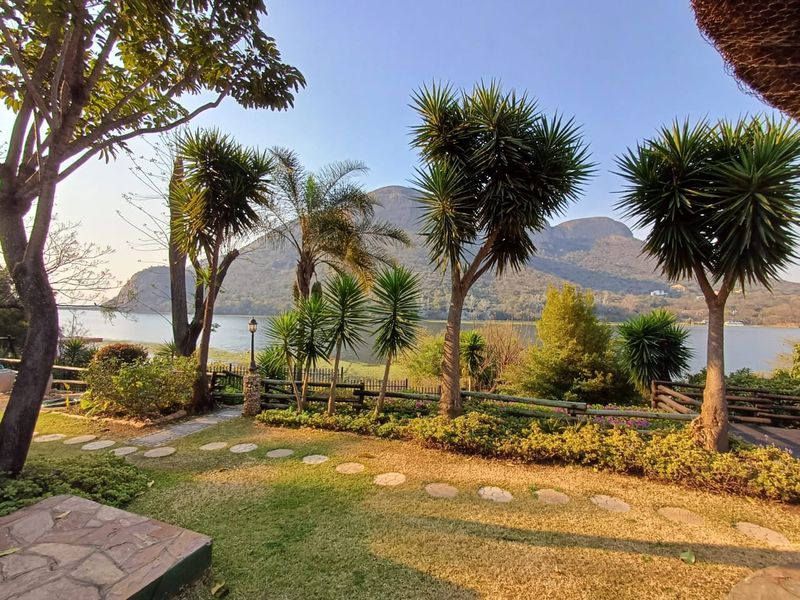 A scenic outdoor view featuring a landscaped garden with stone pathways, timber fencing, and a picturesque backdrop of a lake and mountains.