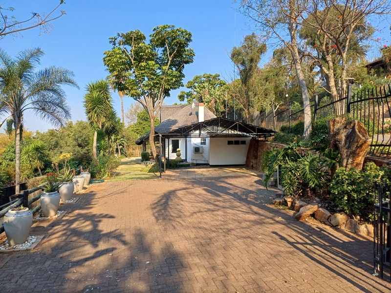 Front view of the property featuring a paved driveway, a covered carport, and a house with a traditional thatched roof set in a landscaped garden.