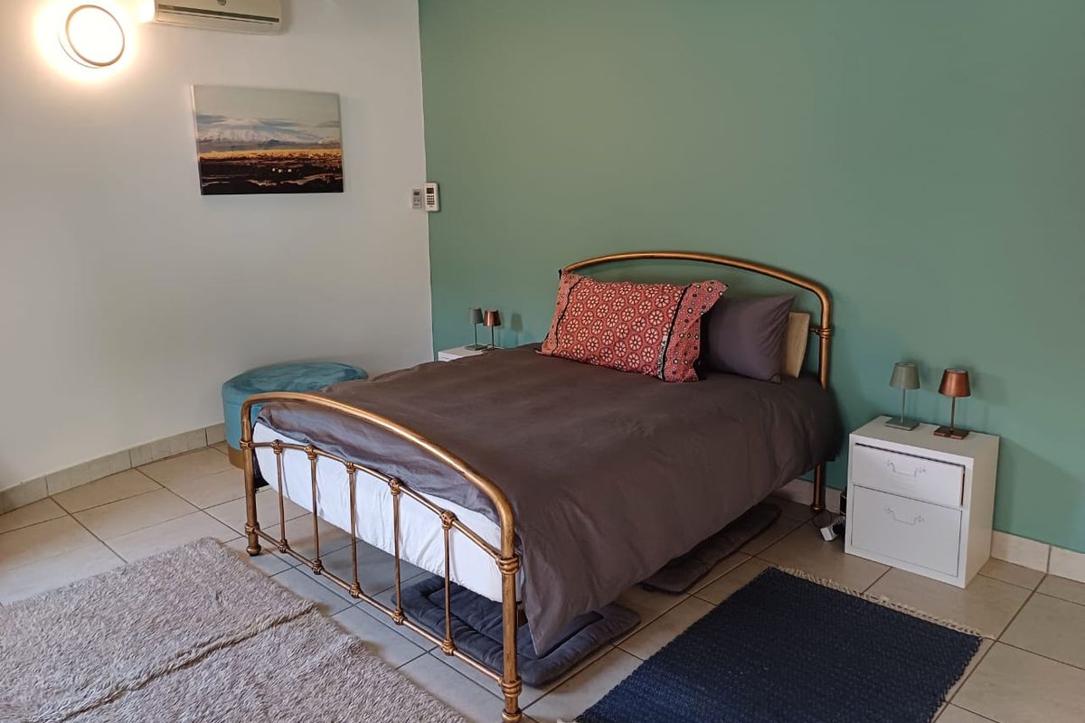 A bedroom featuring tiled flooring, exposed timber ceiling beams, and a wall-mounted air conditioning unit against a green accent wall.