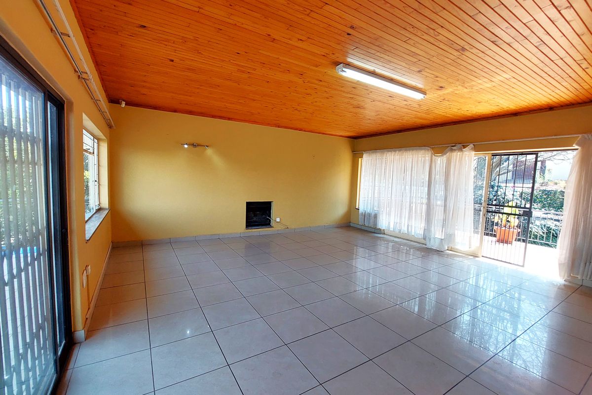 Spacious, empty living area featuring ceramic floor tiles, a timber tongue and groove ceiling, and a built-in fireplace with access to the patio.