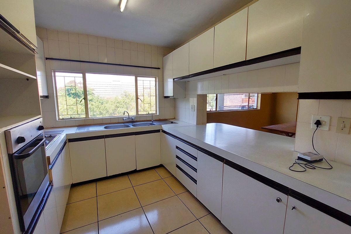 A functional, dated kitchen featuring white cabinetry, built-in oven and hob, double sink, and tiled flooring with ample natural light.