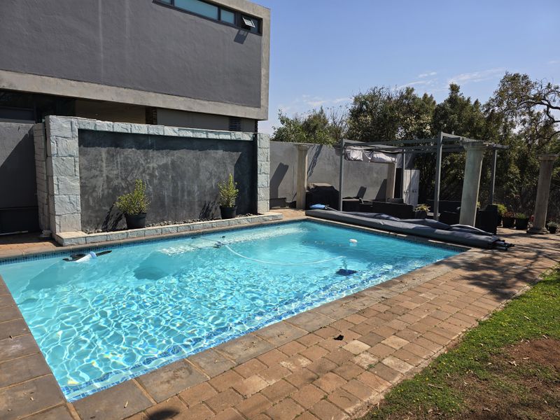 A well-maintained swimming pool area featuring a stone feature wall, paved decking, and a pergola, set against a modern residential building.