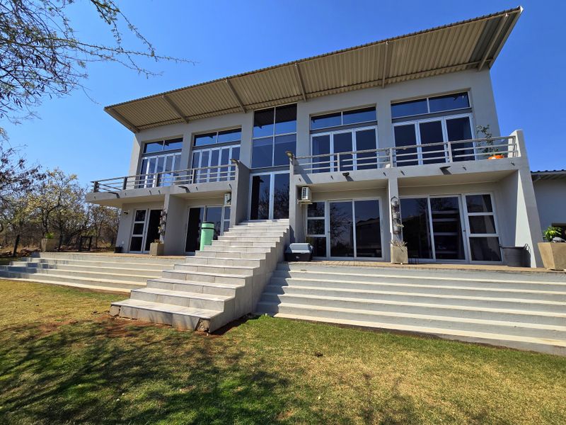 Rear elevation of a modern double-story house featuring a large tiled staircase, expansive glass sliding doors, and a spacious upper balcony.