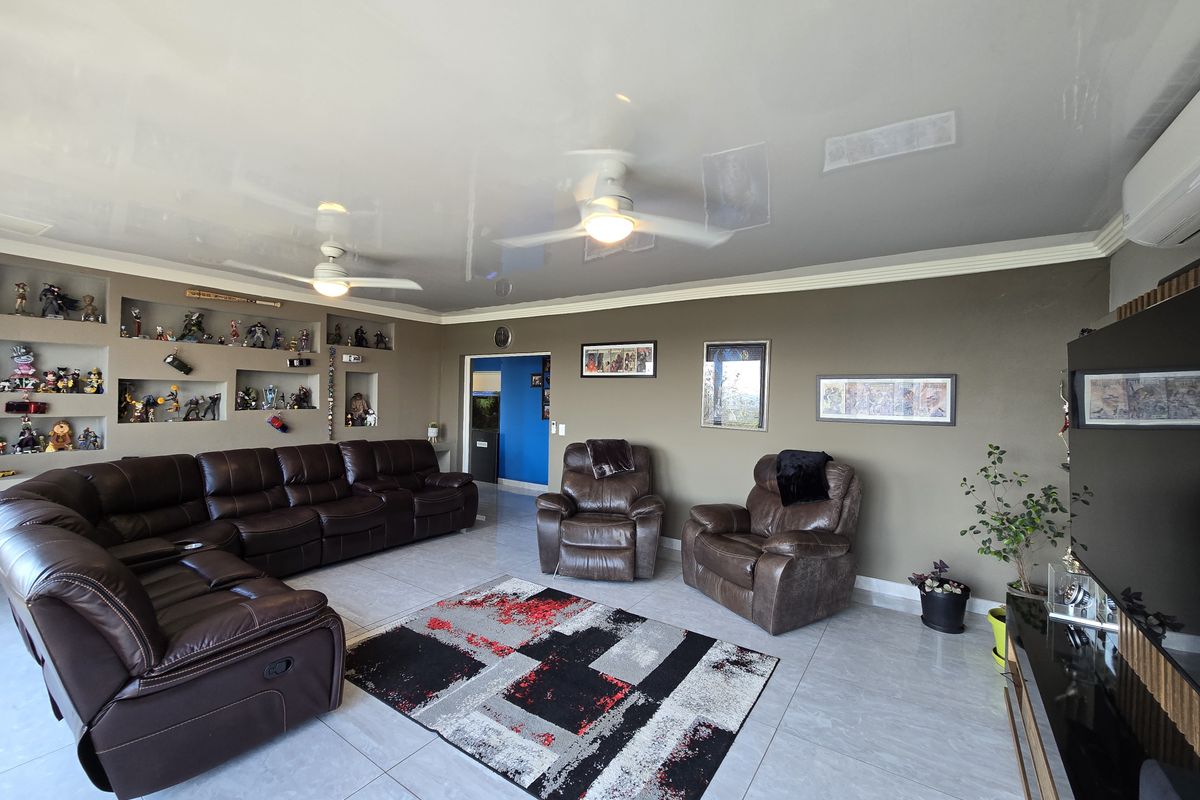 Spacious living room featuring large format floor tiles, recessed wall shelving, dual ceiling fans, and a wall-mounted air conditioning unit.