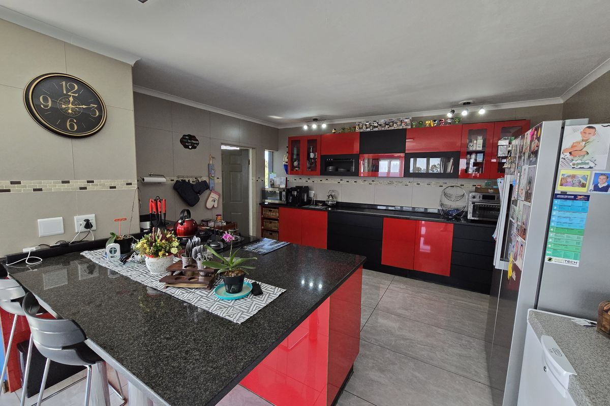 Modern kitchen featuring high-gloss red and black cabinetry, a large granite-topped island, and neutral tiled flooring throughout.