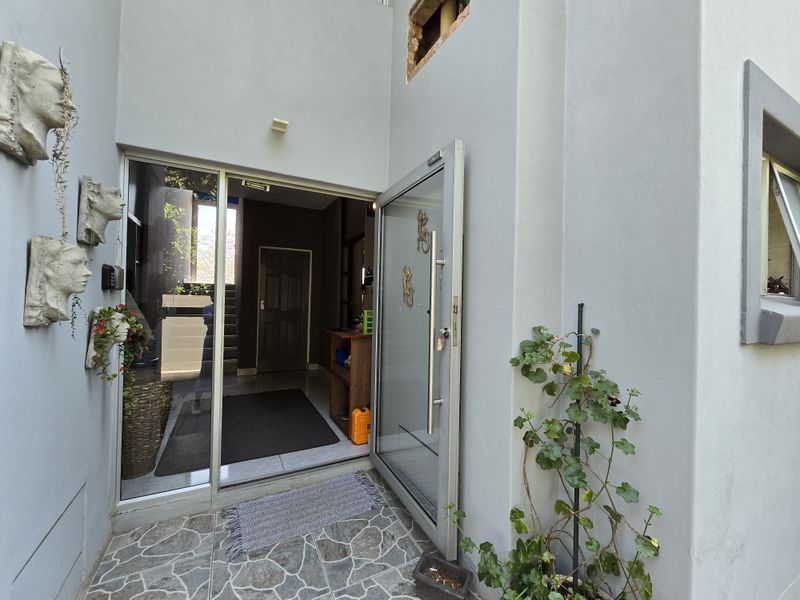 Entrance area featuring a modern glass pivot door, stone tiled flooring, and exterior wall lighting, with some visible masonry work required above the door frame.