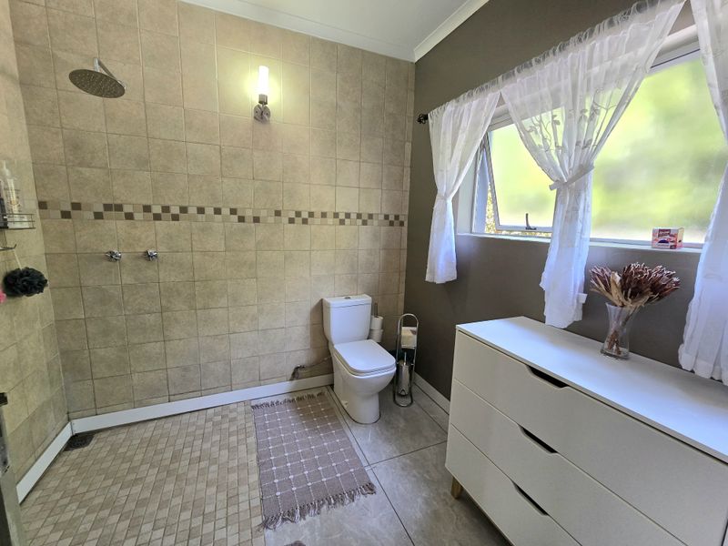 A functional bathroom featuring a walk-in shower with rainfall shower head, tiled wall finishes, and a standard toilet.
