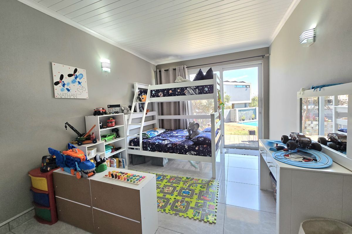 A bright bedroom featuring tiled flooring, a tongue and groove ceiling, and a sliding glass door providing direct access to the outdoor pool area.