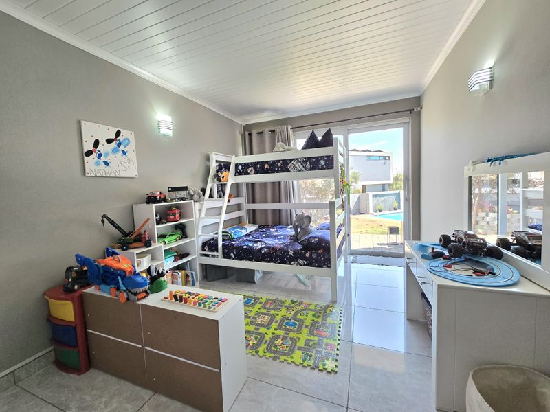 A bright bedroom featuring tiled flooring, a tongue and groove ceiling, and a sliding glass door providing direct access to the outdoor pool area.