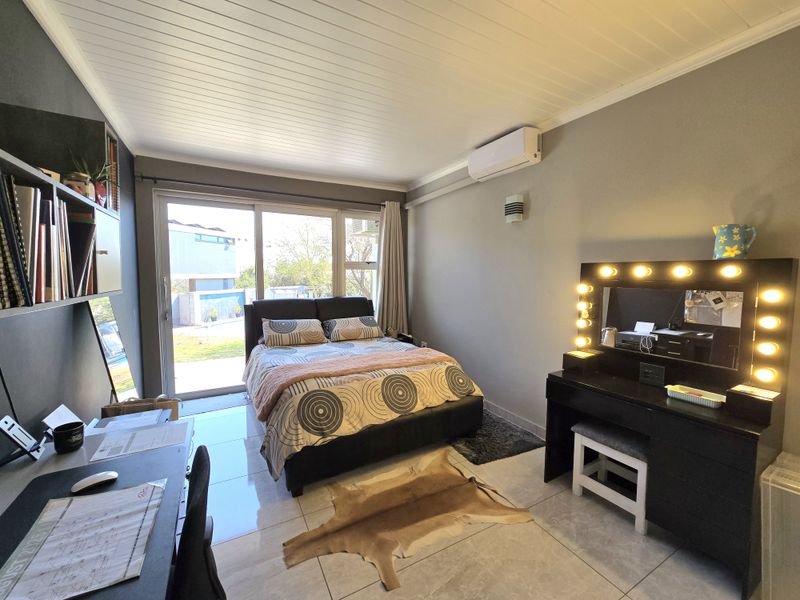 A well-lit bedroom featuring tiled flooring, a split-system air conditioner, and a large sliding glass door providing direct access to the outdoor area.