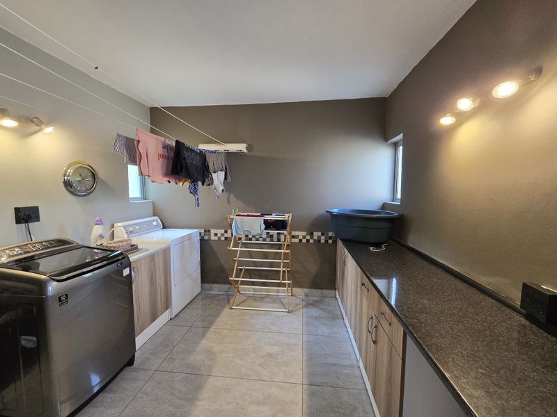 A functional laundry room featuring built-in cabinetry, granite countertops, tiled flooring, and wall-mounted lighting.
