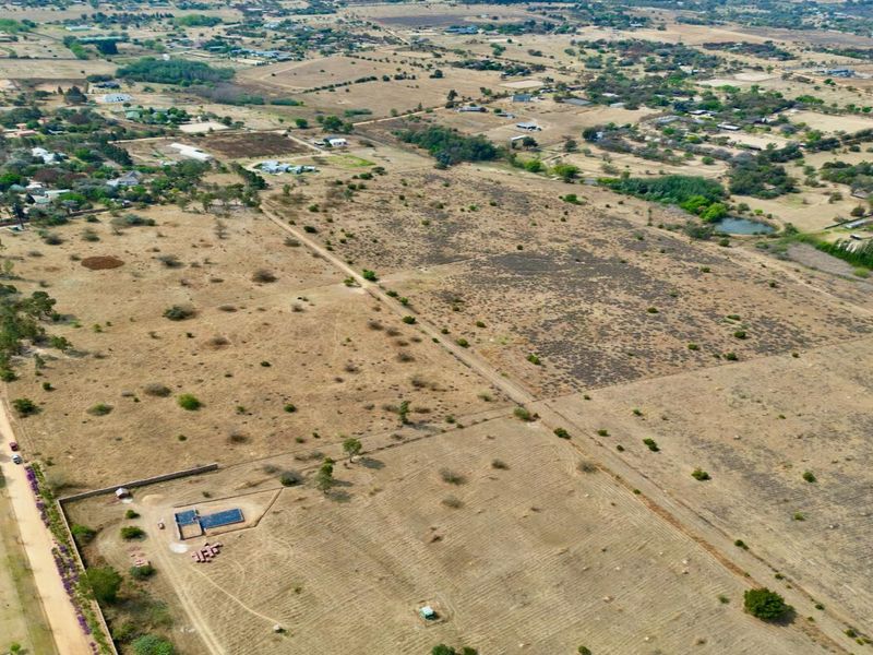 An aerial view of a large, undeveloped residential land plot featuring natural vegetation, perimeter fencing, and access to a dirt road.