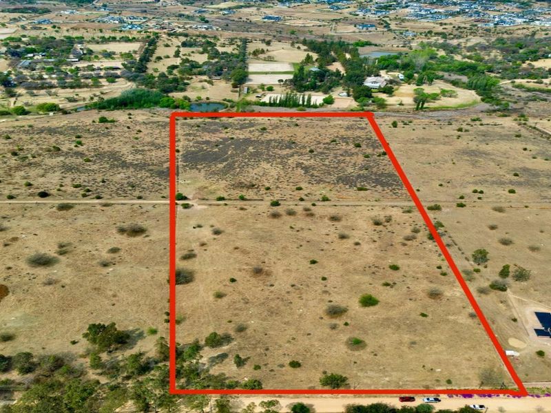 An aerial view of a large, vacant residential plot of land with boundary lines highlighted, situated in a rural estate setting.