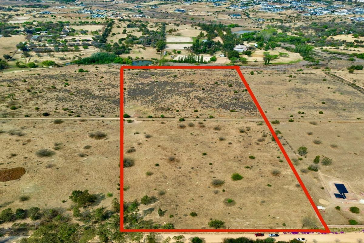An aerial view of a large, vacant residential plot of land with boundary lines highlighted, situated in a rural estate setting.