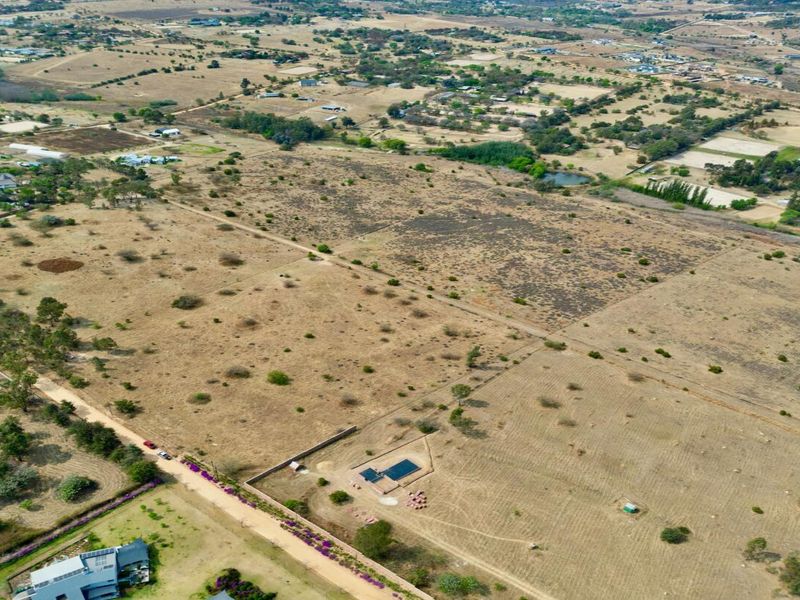 Aerial view of a large, undeveloped residential land parcel featuring natural vegetation, perimeter fencing, and a small existing structure.