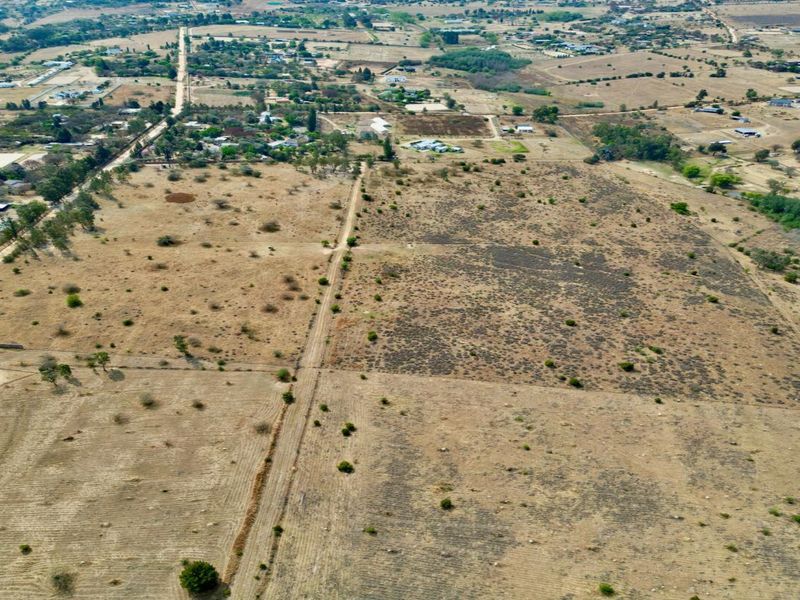 An aerial view of a large, undeveloped residential land parcel featuring dry vegetation, perimeter fencing, and an internal dirt access road.